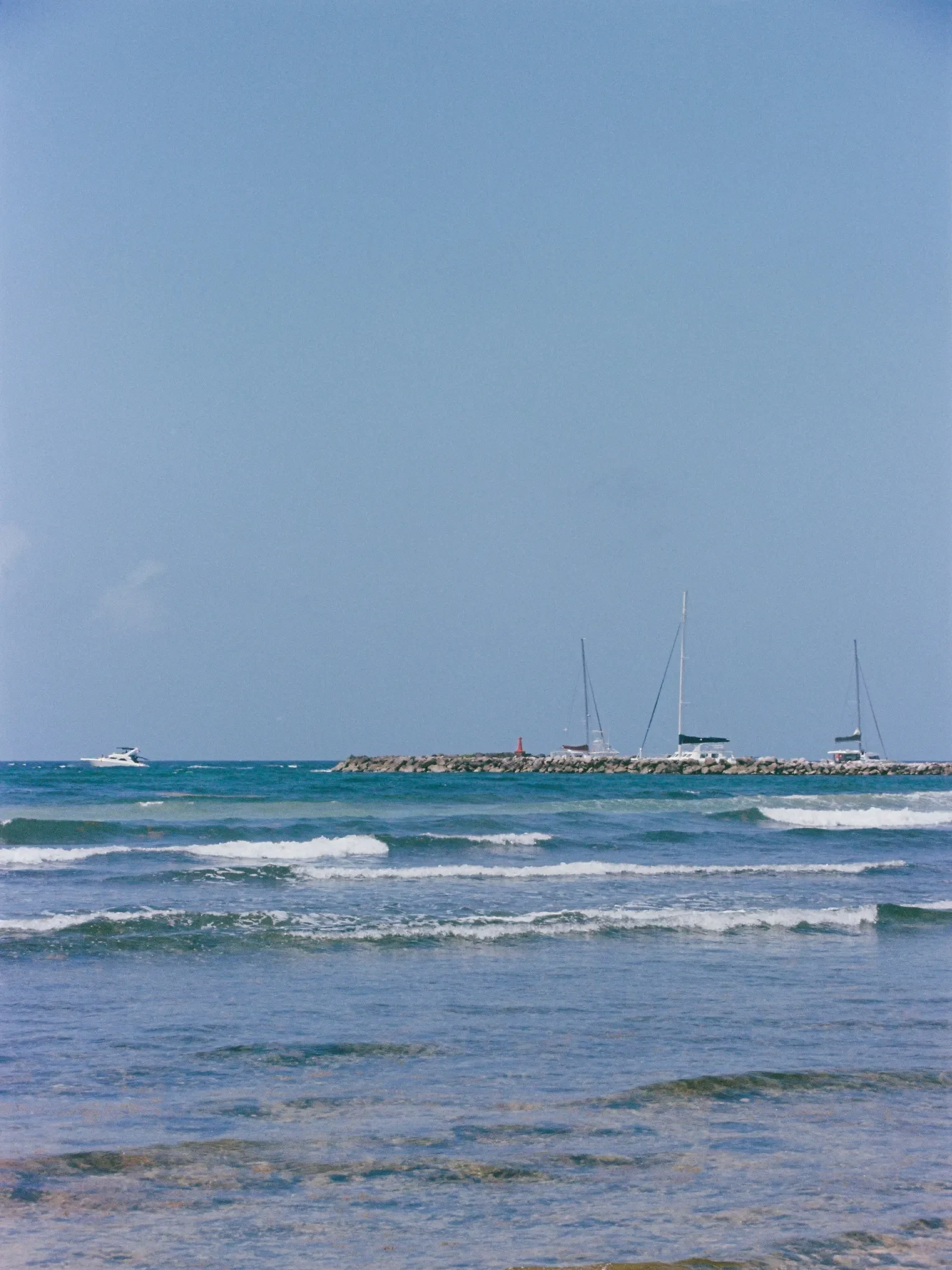 Transporte privado desde el aeropuerto de Cancún a Puerto Aventuras 3 Veleros y una lancha a motor cerca de un rompeolas de rocas en el puerto deportivo de Puerto Aventuras